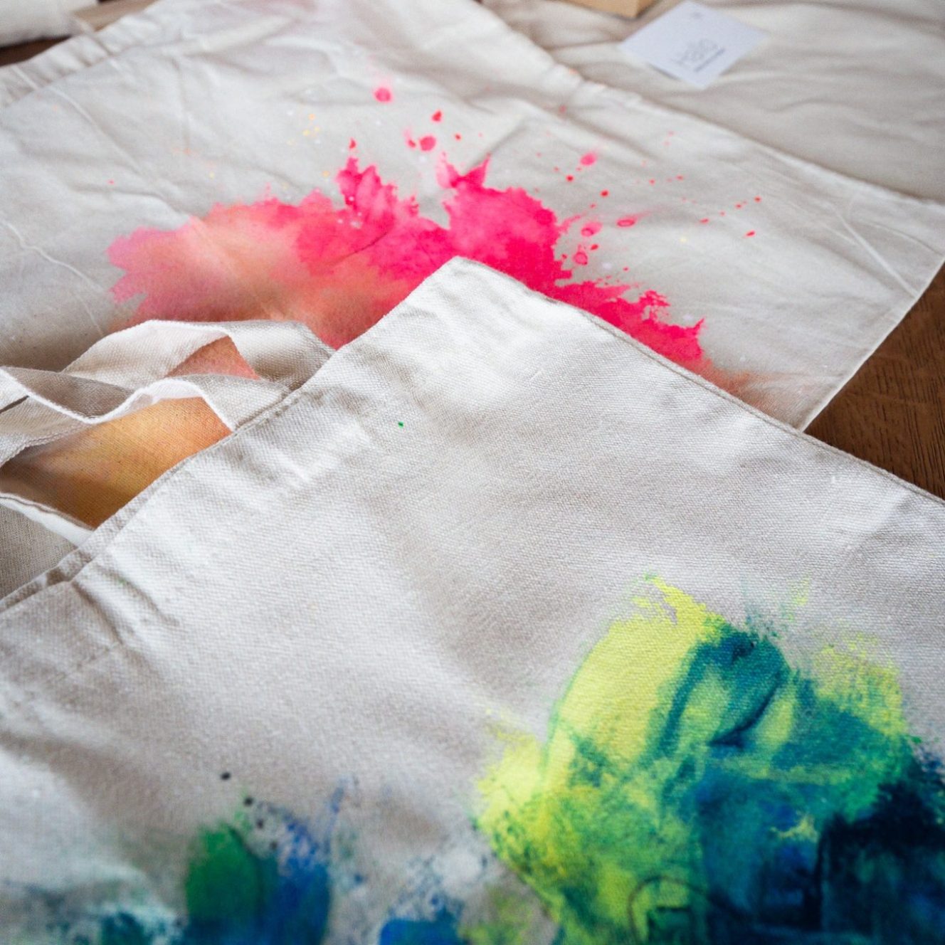 Mehrere Baumwolltaschen auf einem Workshop-Holztisch, umgeben von Zubehör.