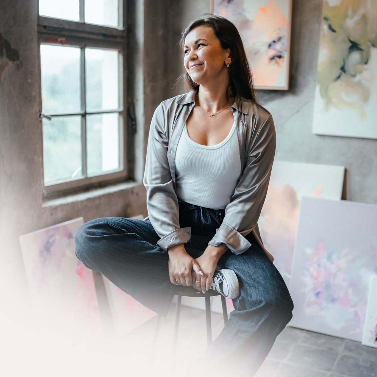 Künstlerin Anca Juliana sitzt in einem Atelier zwischen abstrakten Gemälden.