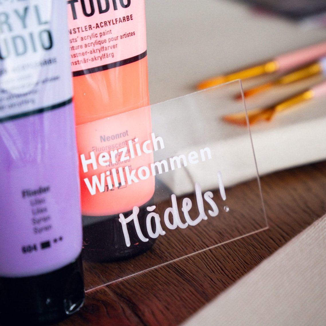 Willkommensschild mit der Aufschrift "Herzlich Willkommen Mädels!" neben Farbtuben.