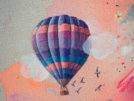 Bunte Heißluftballon fliegt über Wolken und Vögel im Himmel.