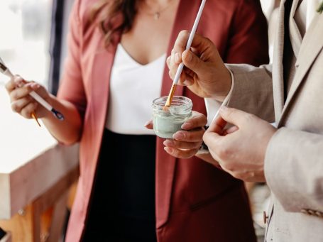 Eine Person mit blonder Haarfarbe geht mit zwei braunen Hunden – Dackeln –am Strand spazieren.