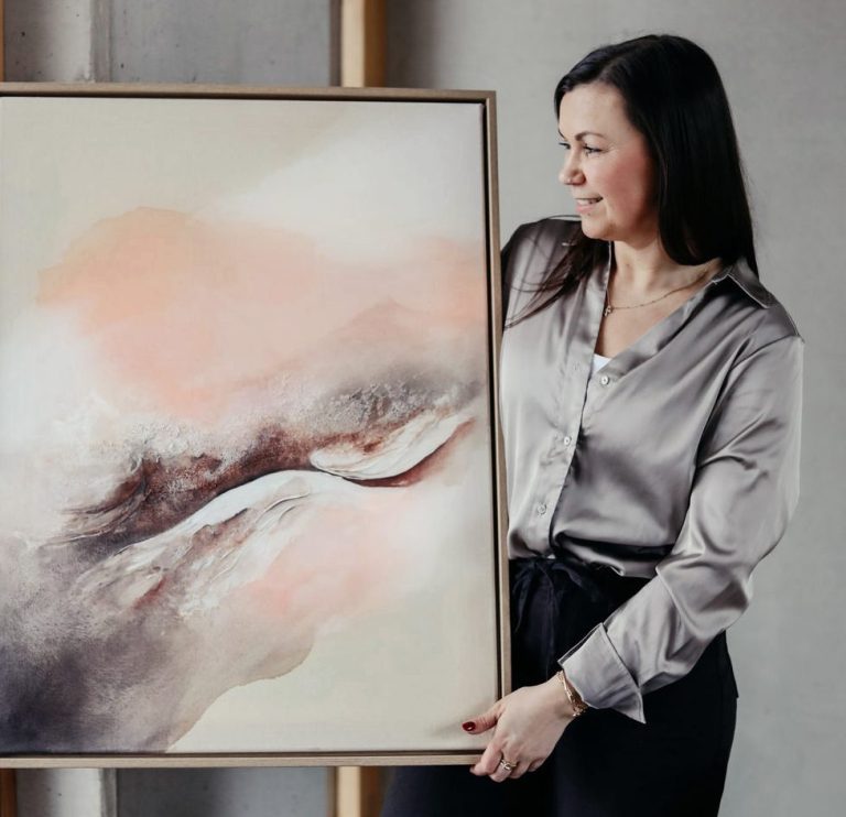 Frau mit langen Haaren steht vor einer leeren Leinwand und hält einen Pinsel.