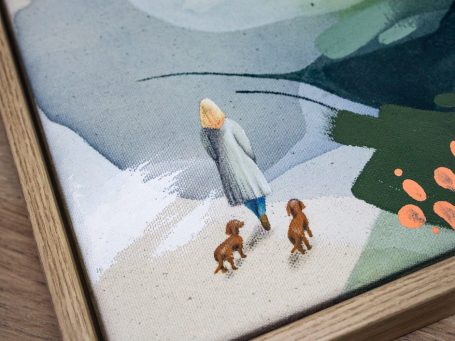 Eine Person mit blonder Haarfarbe geht mit zwei braunen Hunden – Dackeln –am Strand spazieren.