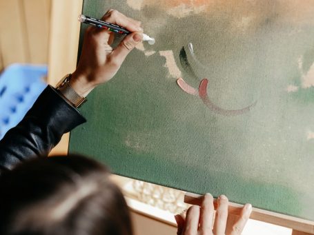 Hände halten einen Pinsel und malen auf einer Leinwand während einer Hochzeit.