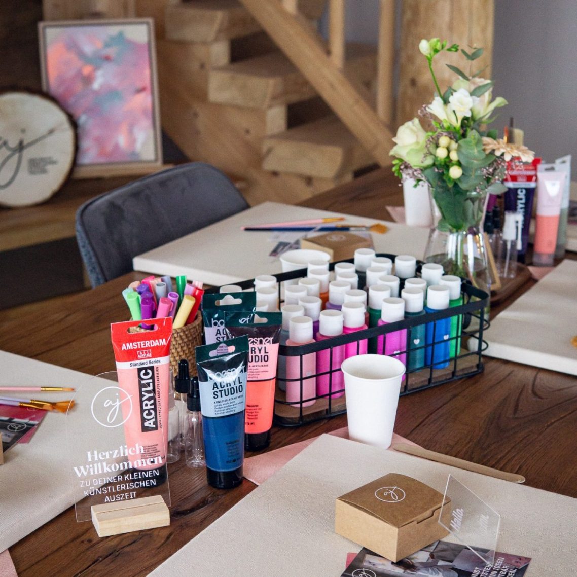 Arbeitsplatz mit Farben, Pinseln, Leinwänden und Blumenarrangement.
