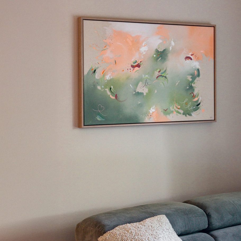 Ein abstraktes Gemälde in sanften Farben, über einer grauen Couch aufgehängt.